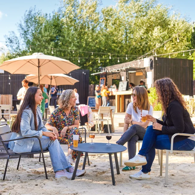 4 femmes assises sur des chaises dans le sable et prenant un verre
