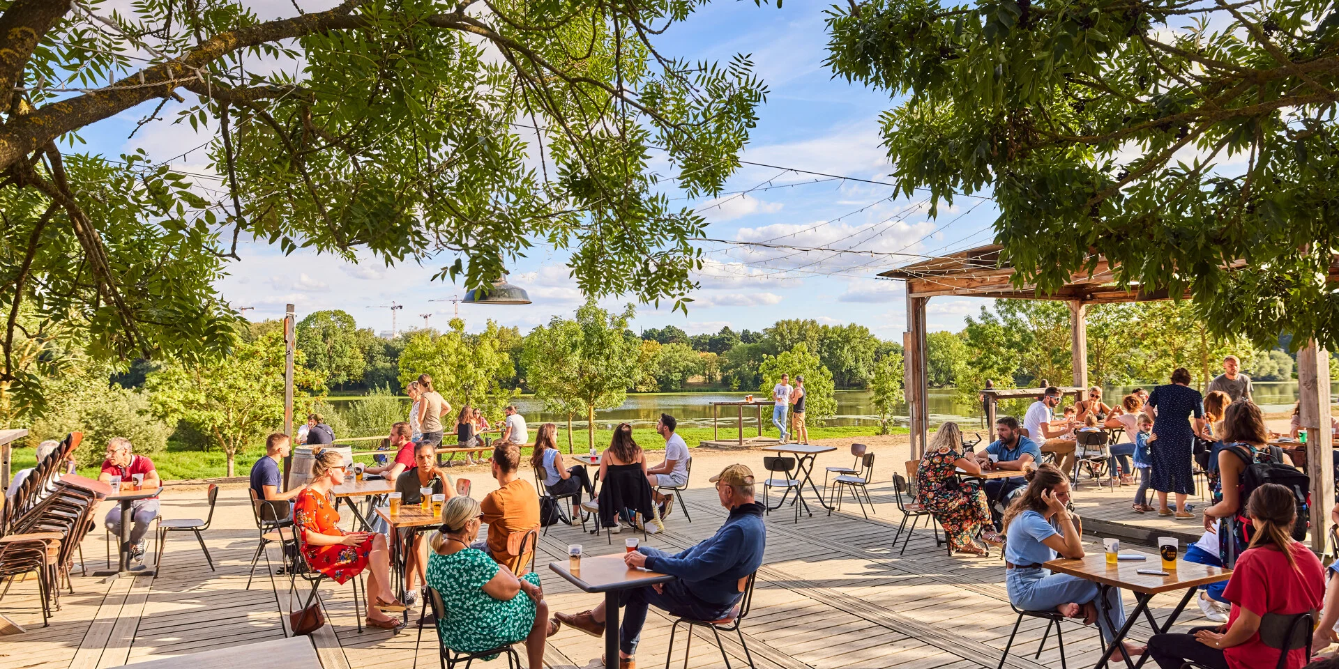 Plan large sur la terrasse et la vue sur la Maine en arrière-plan. Des personnes à tables au premier plan, temps ensoleillé