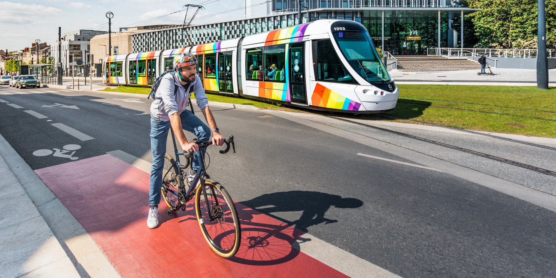 Homme à vélo avec le tram passant derrière, devant le Centre de Congrès d'Angers