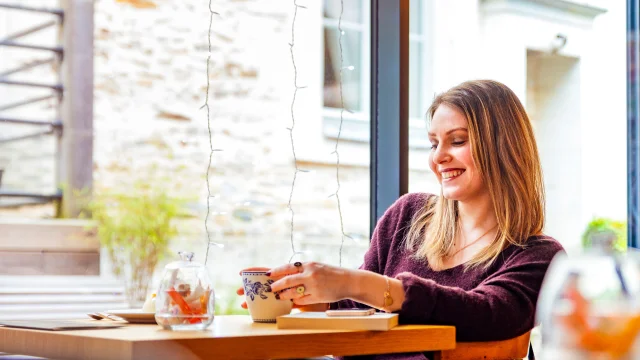 Femme attablée à une table dans un salon de thé angevin en train de déguster son chocolat chaud. ©Christophe Martin