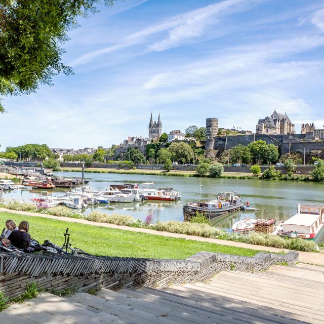 Young people sitting on the grass near the port of Savatte, facing the Maine and the castle of Angers.