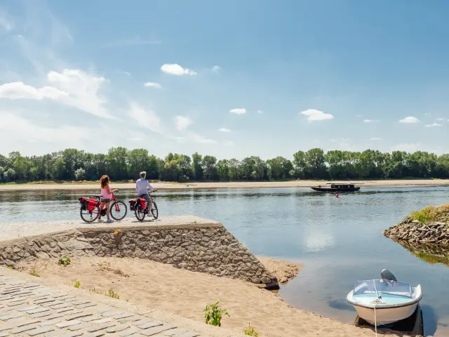 Couple arrêté à vélo au second plan regardant passer sur la Loire une toue