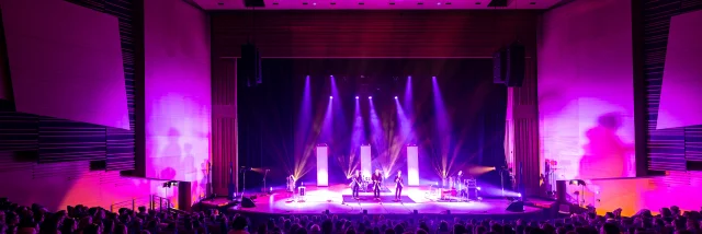 Plan large de la scène du grand auditorium du Centre de congrès éclairée dans les tons violet rose, la salle est comble.