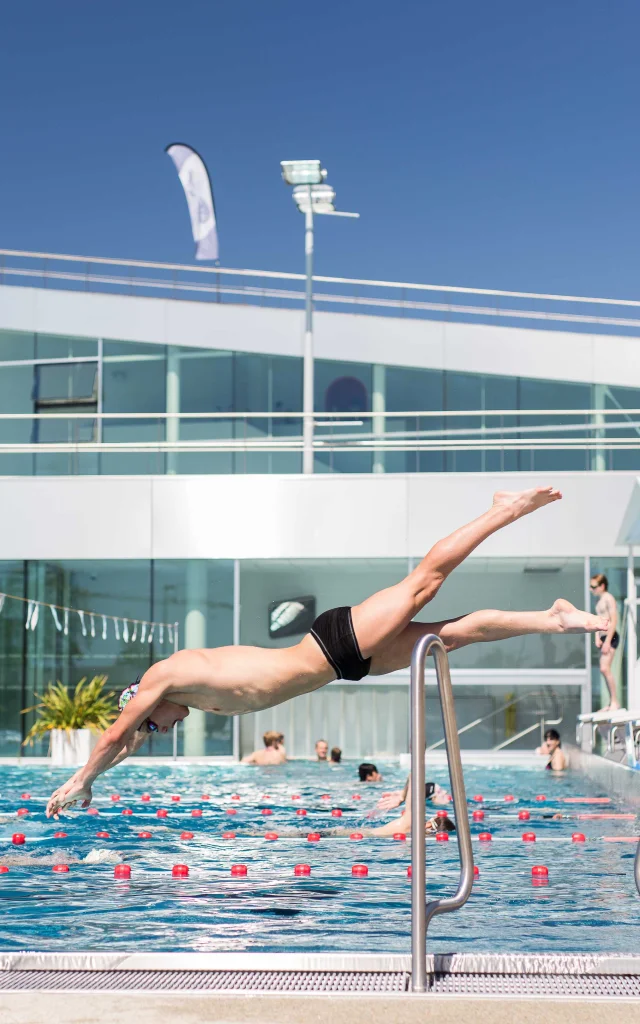 Wide shot of a man diving into the outdoor swimming pool, sunny weather