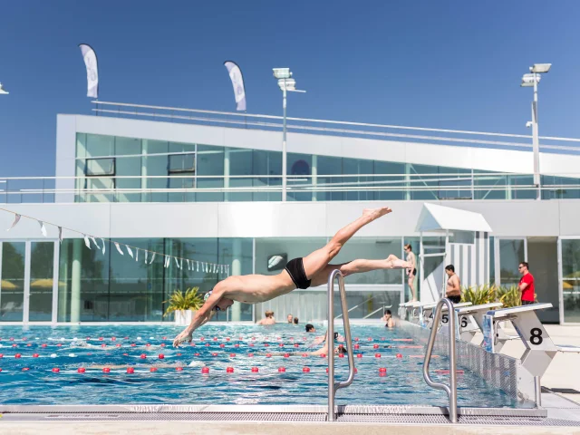 Plan large d'un homme qui plonge dans la piscine extérieure, temps ensoleillé