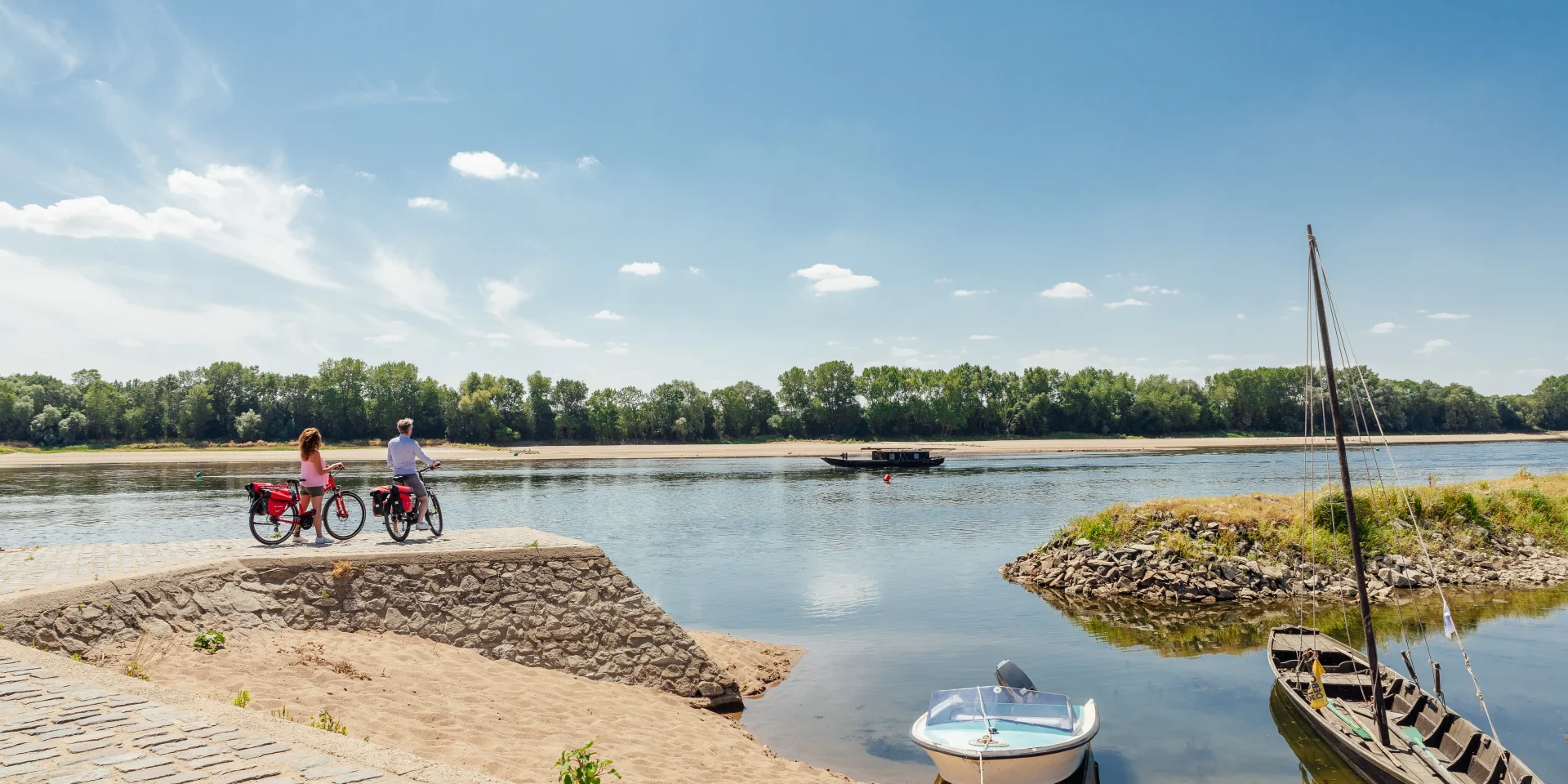 Couple arrêté à vélo au second plan regardant passer sur la Loire une toue