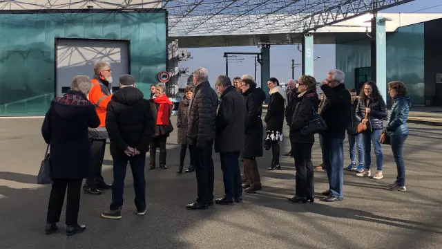 Groupes de personnes rassemblée devant un bâtiment et qui écoutent un homme vêtu de rouge parler