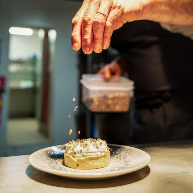 Vue zoomée sur la main d'un chef cuisinier qui termine la préparation d'un dessert sucré