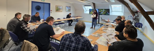Personnes assises dans une salle de réunion, face à deux écrans allumés