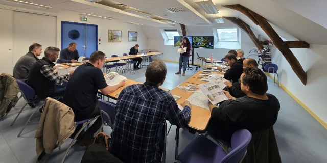 Personnes assises dans une salle de réunion, face à deux écrans allumés