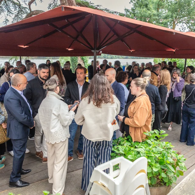 Nombreuses personnes discutant sous un grand parasol en extérieur