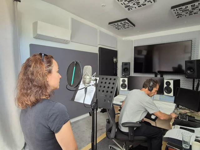 Jeune femme devant un micro, homme devant une table de mixage au second plan