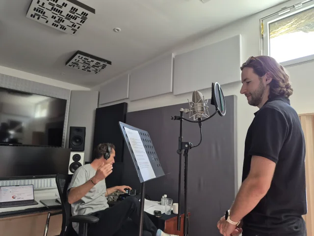 Jeune homme devant un micro, homme devant une table de mixage au second plan