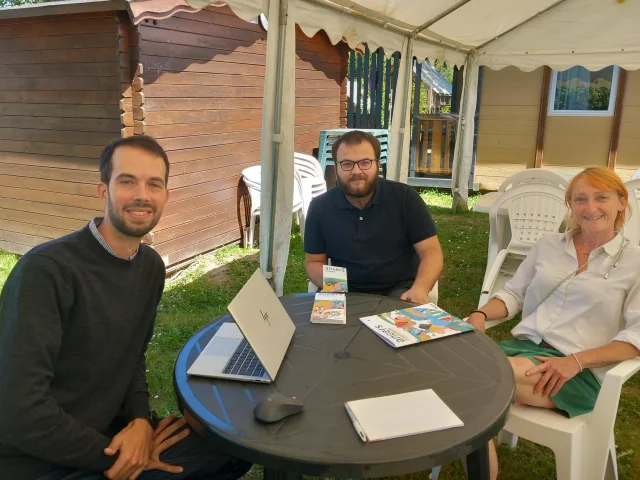 3 personnes assises autour d'une table en extérieur et regardant l'objectif